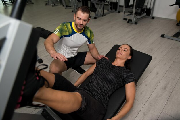 Foto mujer entrena piernas en máquina con entrenador personal