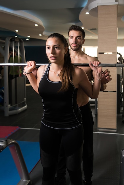 Mujer con entrenador personal en sentadilla con barra