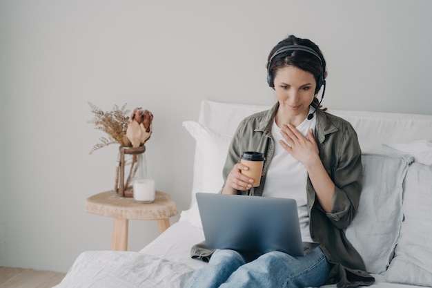 Mujer entrenadora de vida en auriculares realiza consultas en línea por videollamada en una computadora portátil en el dormitorio en casa