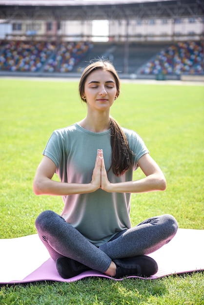 Mujer entrenando al aire libre. Ella está sentada en una colchoneta sobre la hierba verde y hace ejercicios de yoga.