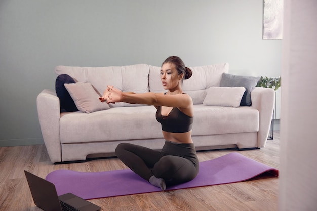 Mujer entrenando en casa y viendo videos en una laptop chica haciendo ejercicio en la sala de estar