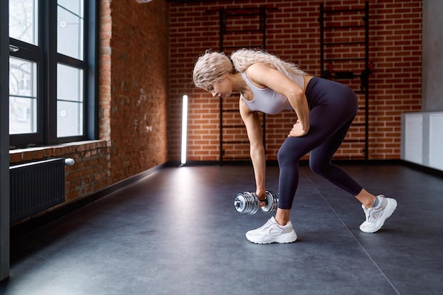 Mujer entrenando con pesas en el gimnasio. Chica culturista practicando sentadillas con pesas bombeando nalgas