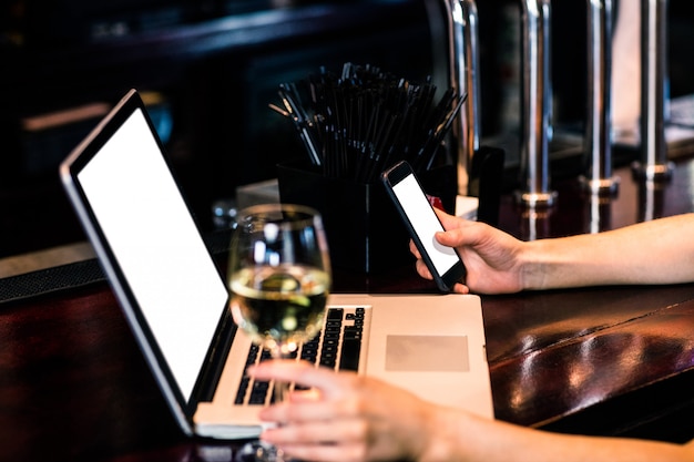 Mujer enviando mensajes de texto y usando una computadora portátil con vino en un bar
