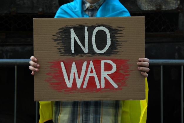 Mujer envuelta en bandera ucraniana sosteniendo un cartel con palabras No War on street closeup