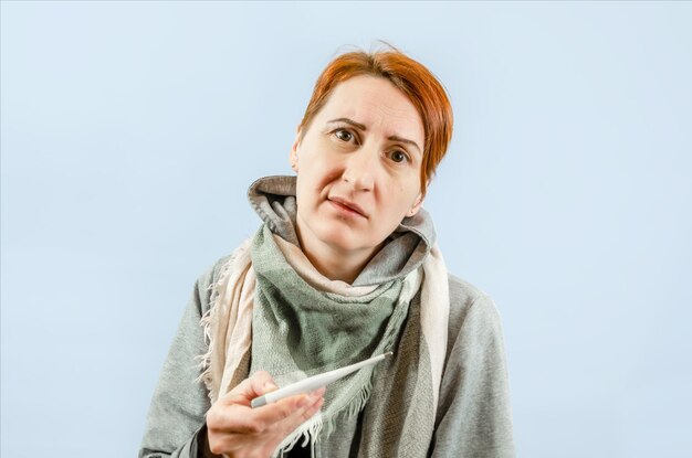 Mujer envuelta en ropa de abrigo sostiene termómetro Expresión facial disgustada fría
