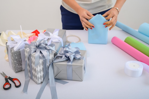 Una mujer envuelve los regalos de Navidad en papel de regalo y ata un lazo de cinta Primer plano de las manos de una mujer preparando sorpresas para el nuevo año Flujo de trabajo de un derator Escritorio