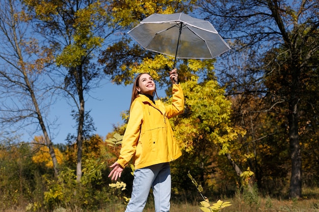 Una mujer es feliz con un paraguas transparente en otoño en un clima soleado