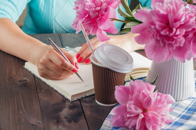 Mujer escribe en el cuaderno, flores en la mesa