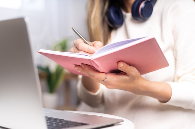 Mujer escribe en un cuaderno con un portátil