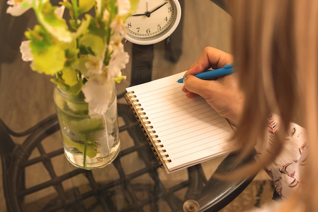 La mujer escribe en el cuaderno sobre el concepto de foto de espacio de trabajo acogedor con vista al hombro con mesa de vidrio