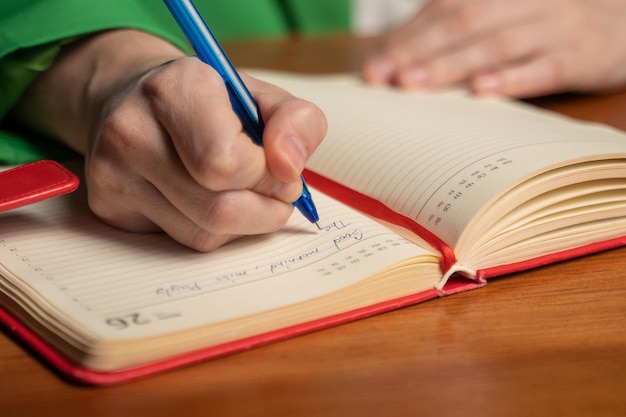 La mujer escribe el horario de trabajo en el diario sentado en la mesa