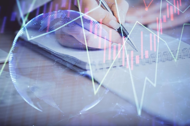 Una mujer escribe información sobre el mercado de valores en el bloc de notas. Hologramas de gráficos Forex delante Concepto de investigación Exposición múltiple