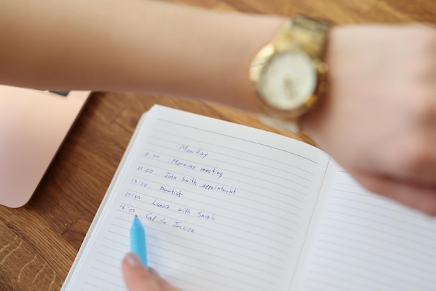 La mujer escribe el plan para el día mira el reloj de pulsera para comprobar la hora