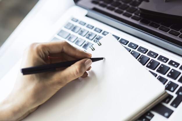 Foto mujer escribe con una pluma en el diario en el teclado de la computadora portátil en una oficina soleada concepto de negocios y educación close up