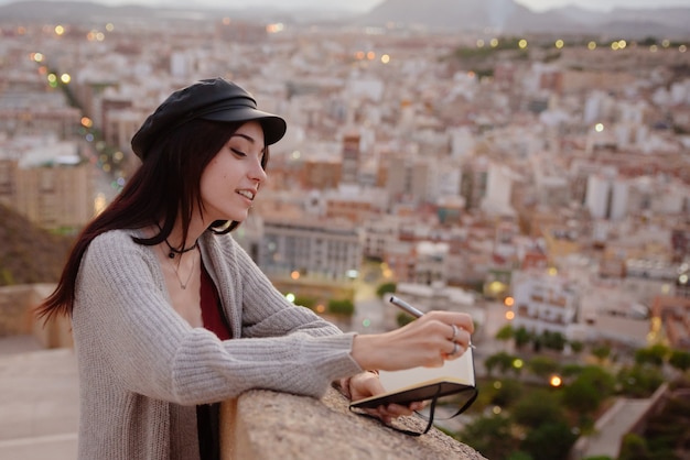 Mujer escribe en su cuaderno frases y pensamientos al aire libre al atardecer