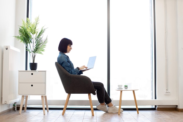 Mujer escribiendo en la computadora portátil mientras está sentada en el sillón de la oficina
