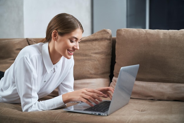 Mujer escribiendo en la computadora portátil mientras se relaja en el sofá