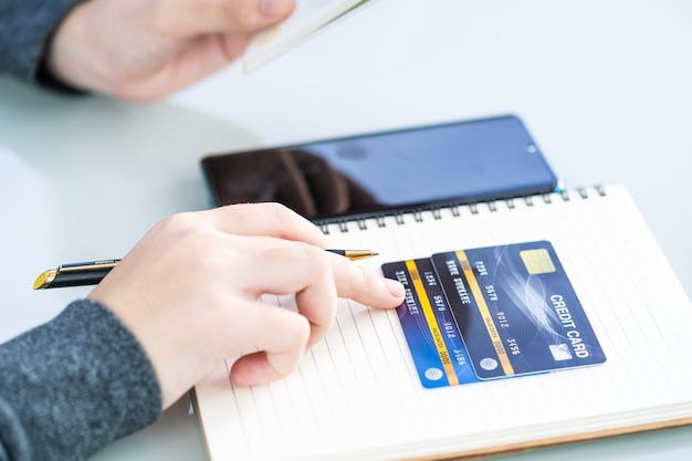 Mujer escribiendo en el cuaderno con tarjeta de crédito y escritorio de teléfono inteligente