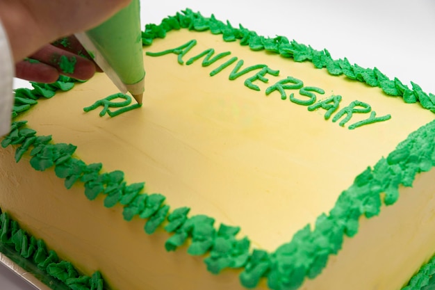 Mujer escribiendo con manga pastelera en pastel de cumpleaños verde y amarillo aislado sobre fondo blanco.