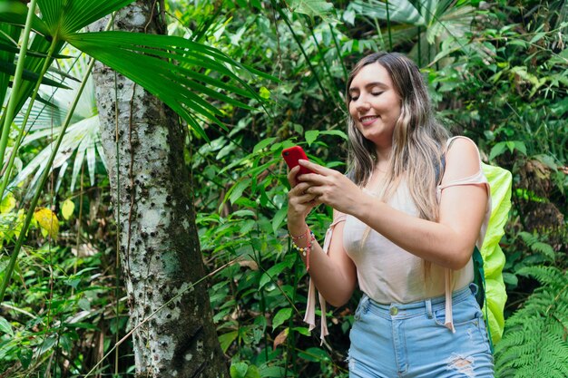 Mujer escribiendo un mensaje con su teléfono celular en un bosque tropical