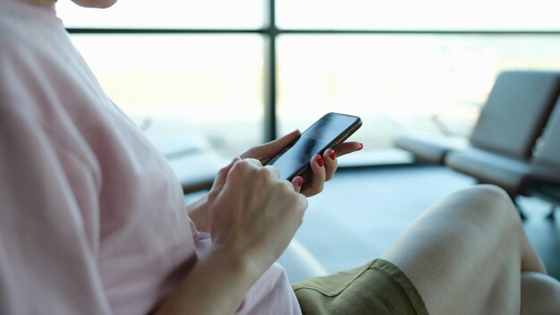 Mujer escribiendo un mensaje en el teléfono móvil en el primer plano del edificio del aeropuerto