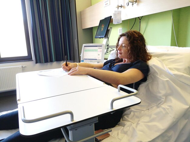 Foto mujer escribiendo mientras está sentada en la cama en el hospital