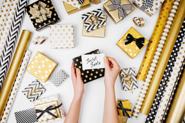 Mujer escribiendo tarjeta de felicitación para regalos de Navidad. Fondo de decoración navideña en colores dorado y negro. Endecha plana, vista superior