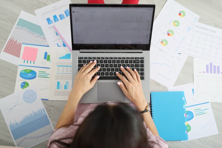 Foto mujer escribiendo en el teclado de la computadora portátil entre un conjunto de documentos vista superior