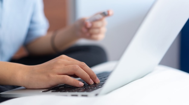Mujer escribiendo en el teclado del ordenador portátil con tarjeta de crédito para pagar el comercio electrónico de compras en línea