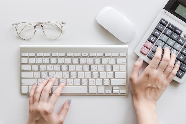 Mujer escribiendo en el teclado, usando calculadora, gafas y mouse