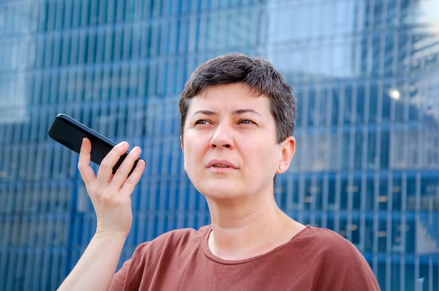 Mujer escucha el mensaje de voz poniendo el teléfono inteligente a su oreja contra el fondo de la fachada de vidrio azul