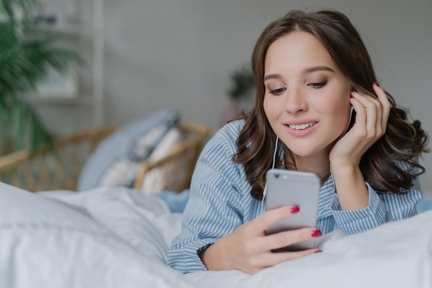 La mujer escucha música, hace videollamadas, se acuesta en la cómoda cama por la mañana, vestida casualmente.