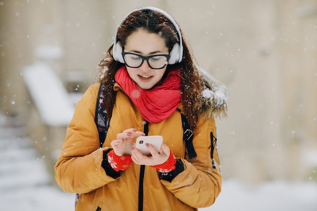 Mujer escucha música en el teléfono móvil en la ciudad en invierno. Retrato de primer plano joven en la ciudad de invierno, sonriendo