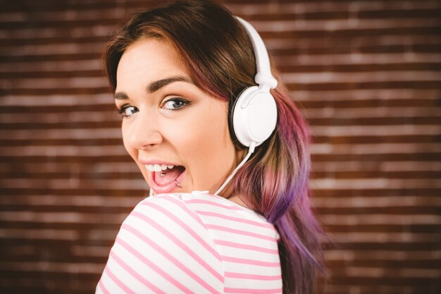 Mujer escuchando música con auriculares contra la pared de ladrillo