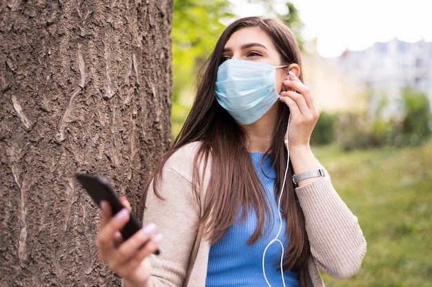 Foto mujer escuchando música en los auriculares mientras usa una máscara médica