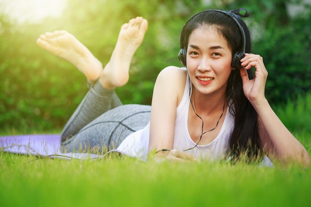 mujer escuchando música con auriculares y tendido en un campo de hierba