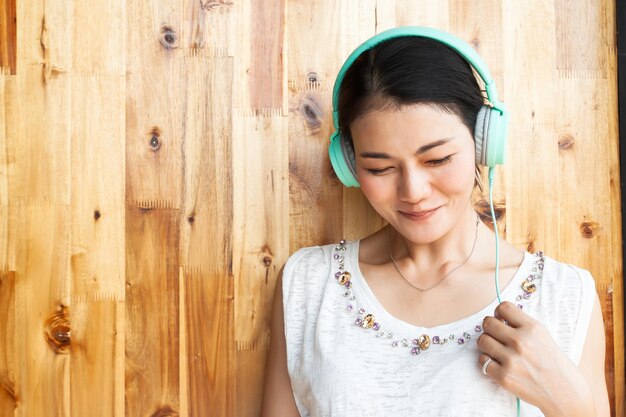 Foto mujer escuchando música contra una pared de madera