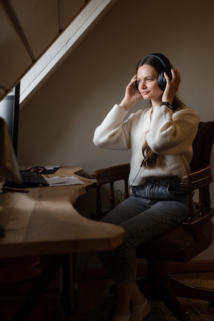 Mujer escuchando música en grandes auriculares cerca de la computadora