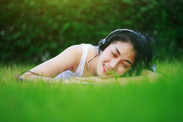 mujer escuchando música mientras sus ojos se cierran con auriculares en campo de hierba