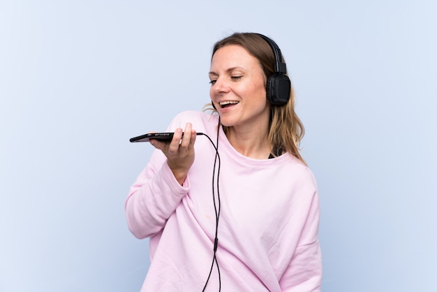 Mujer escuchando música sobre pared azul aislado