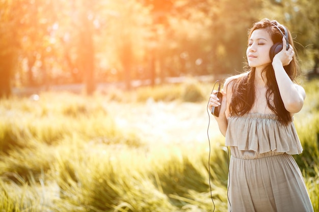 Foto mujer escuchando música a través de auriculares mientras está de pie en el campo