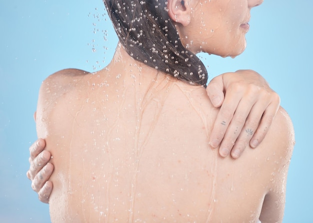 Mujer de espalda y ducha para el cuidado de la piel limpia e higiene contra el fondo azul del estudio Niña y gotas líquidas para lavar el cuidado del cuerpo o la belleza natural para el bienestar, las salpicaduras de agua o la relajación