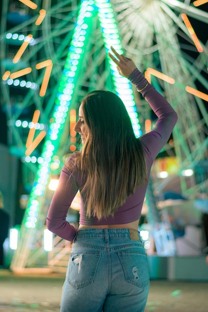 Mujer de espaldas con las luces de una rueda de la fortuna al fondo