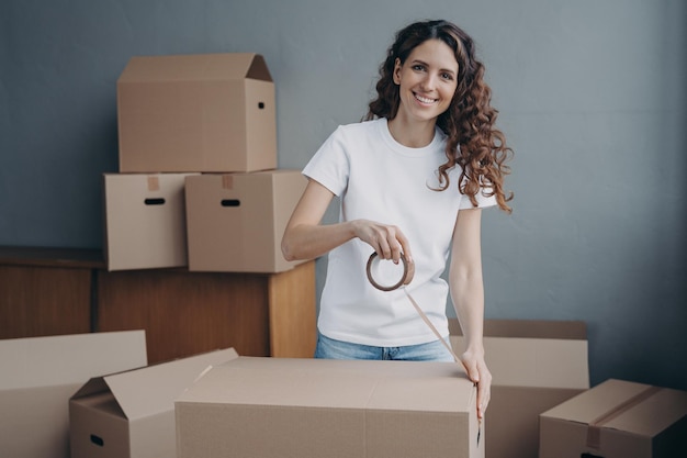 Mujer española sonriente empacando cosas en una caja de cartón usando cinta adhesiva Servicio de retiro de entrega