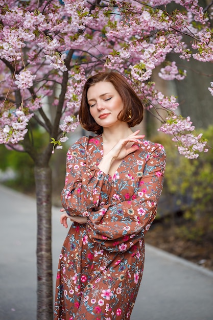 Una mujer espectacular con un vestido brillante se encuentra en el contexto de sakura. Una mujer de cabello oscuro con un hermoso traje sonríe en la calle mientras camina