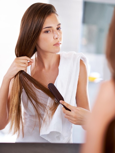 Mujer espejo y cepillo de cabello en el baño en casa para el cuidado de la belleza o rutina matutina con cosméticos Peinado de reflejo y persona seria peinado para la limpieza cuidado o tratamiento para el bienestar