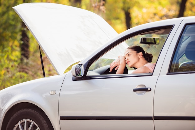 Una mujer espera ayuda cerca de su automóvil averiado en el lado de la carretera