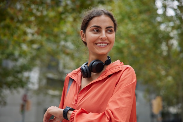 La mujer espera a que alguien en la calle compruebe el tiempo en el reloj inteligente que va a tener entrenamiento deportivo vestida con ropa deportiva