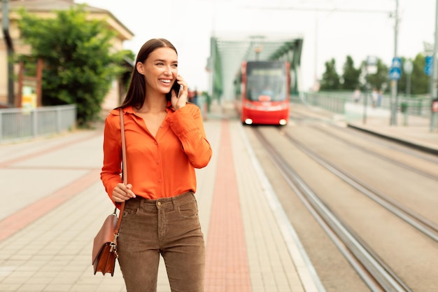 Mujer esperando el tranvía hablando por teléfono en zona urbana