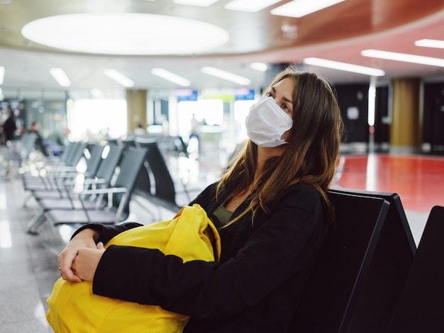 Mujer esperando un vuelo en la máscara médica de la mochila amarilla del aeropuerto